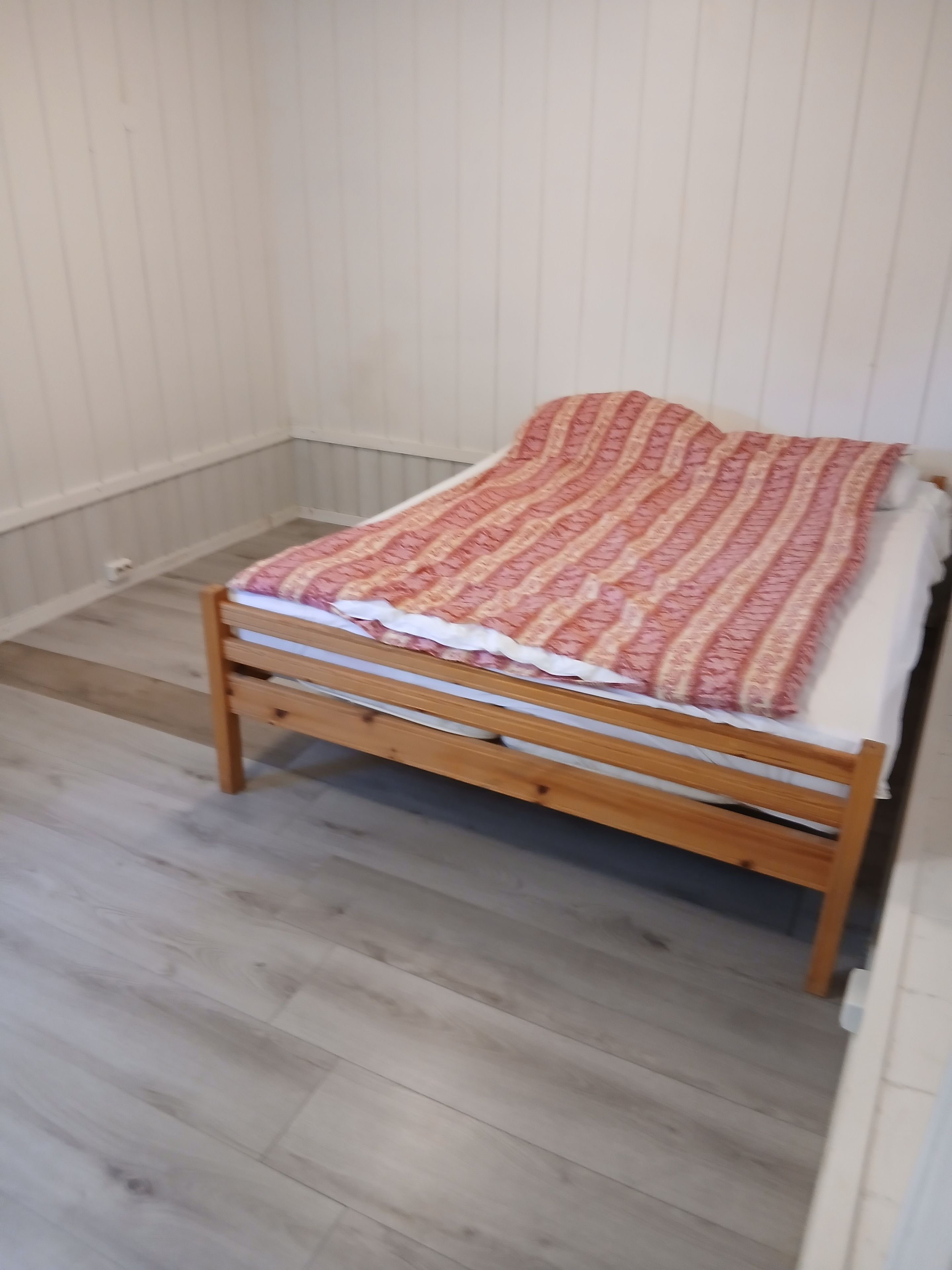 Een eenpersoonsbed met een bedekker met patroon in een kamer met houten vloeren en witte muren.