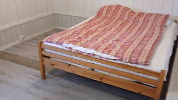 Een eenpersoonsbed met een bedekker met patroon in een kamer met houten vloeren en witte muren.