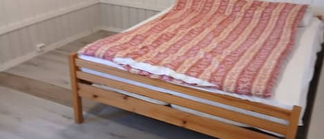 Una cama individual con una colcha estampada en una habitación con piso de madera y paredes blancas.