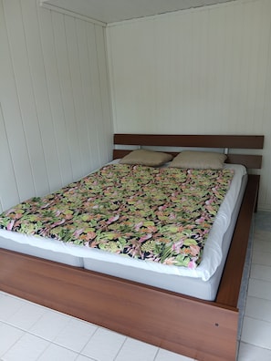 Uma cama com colcha florida, cabeceira de madeira e duas almofadas.