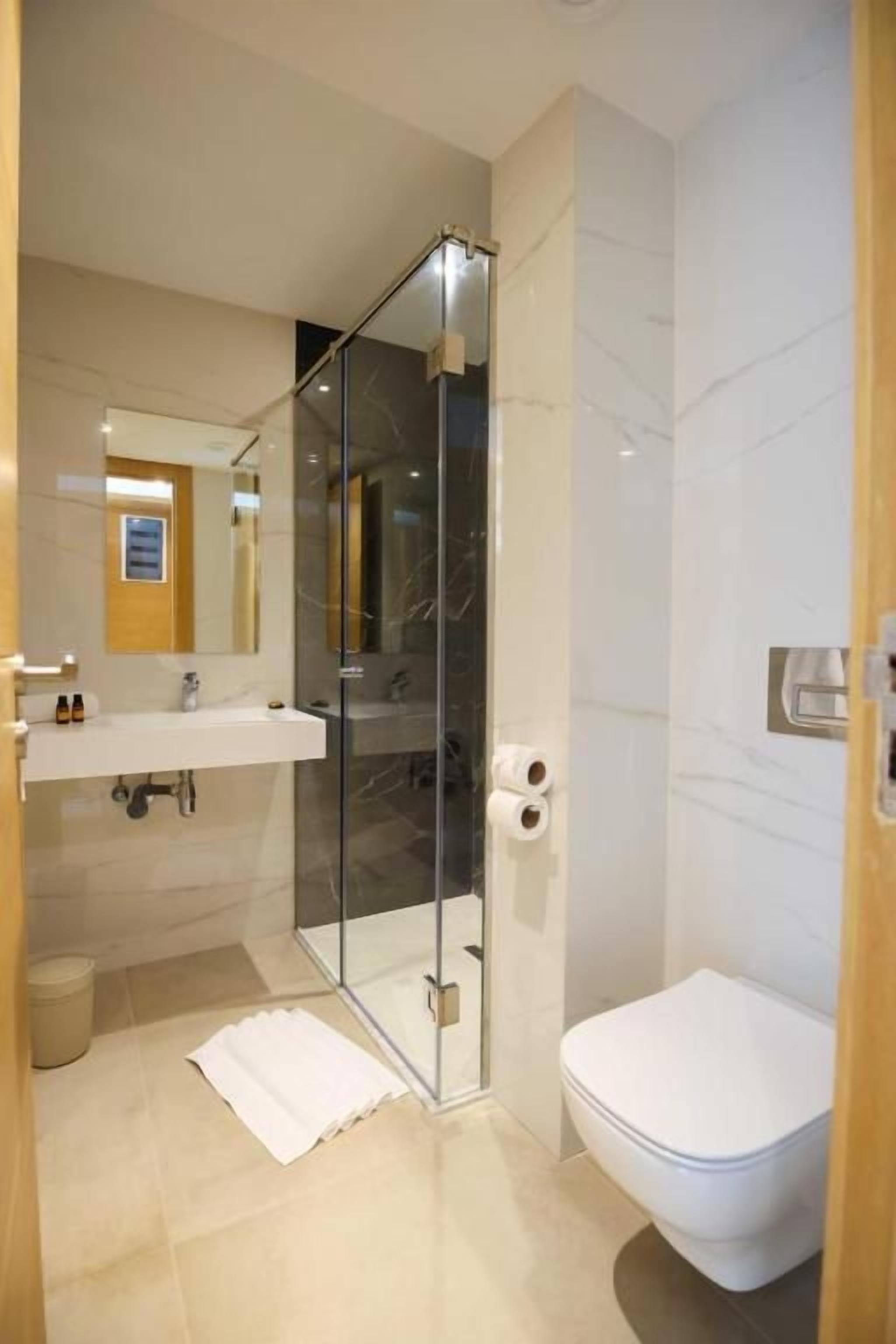 Un baño moderno con cabina de ducha de vidrio, inodoro blanco y lavamanos con espejo.