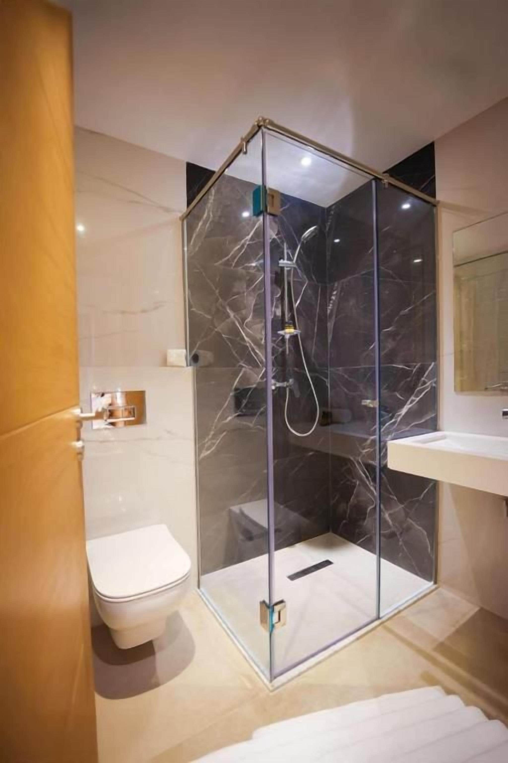 A modern bathroom with a glass-enclosed shower, a toilet, and a vanity with a mirror.