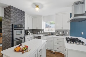 A modern kitchen with white cabinetry, a brick accent wall, stainless steel appliances, and a marble countertop.
