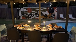 An outdoor dining area with tables set for four, each with a candle and napkin. A mural depicting a cityscape and a bison is visible in the background.