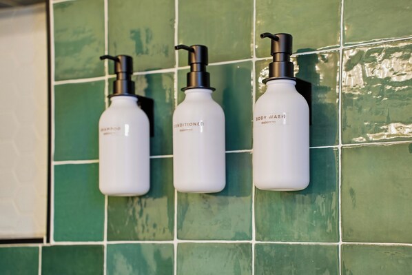 Three white bottles with black pumps on a green tiled wall.