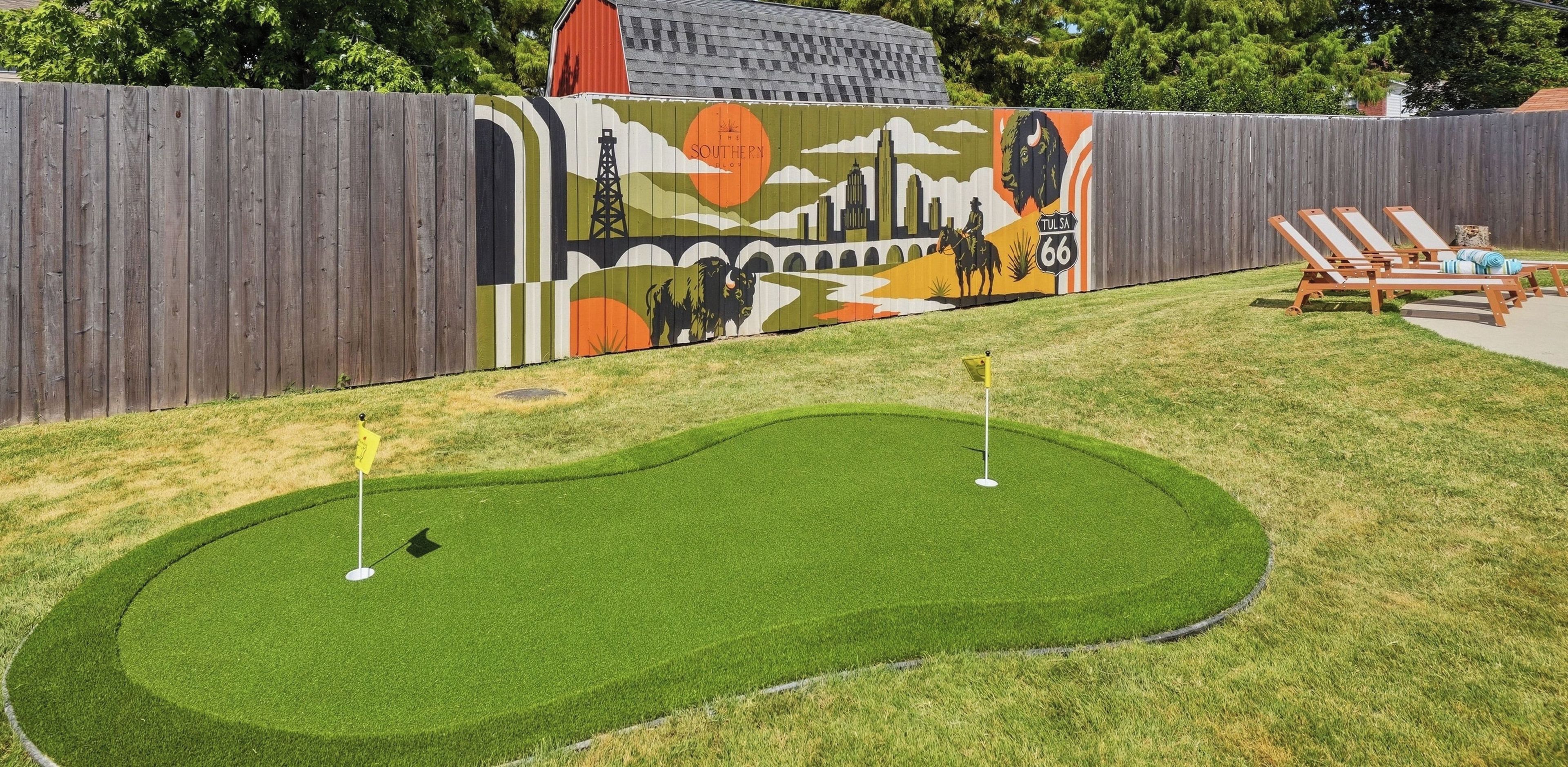 A miniature golf course with two holes, a wooden fence, and a mural in the background.