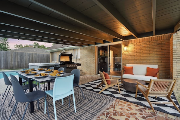 An outdoor patio with a dining table set for four, surrounded by chairs, a barbecue grill, and a seating area with a sofa and chairs.