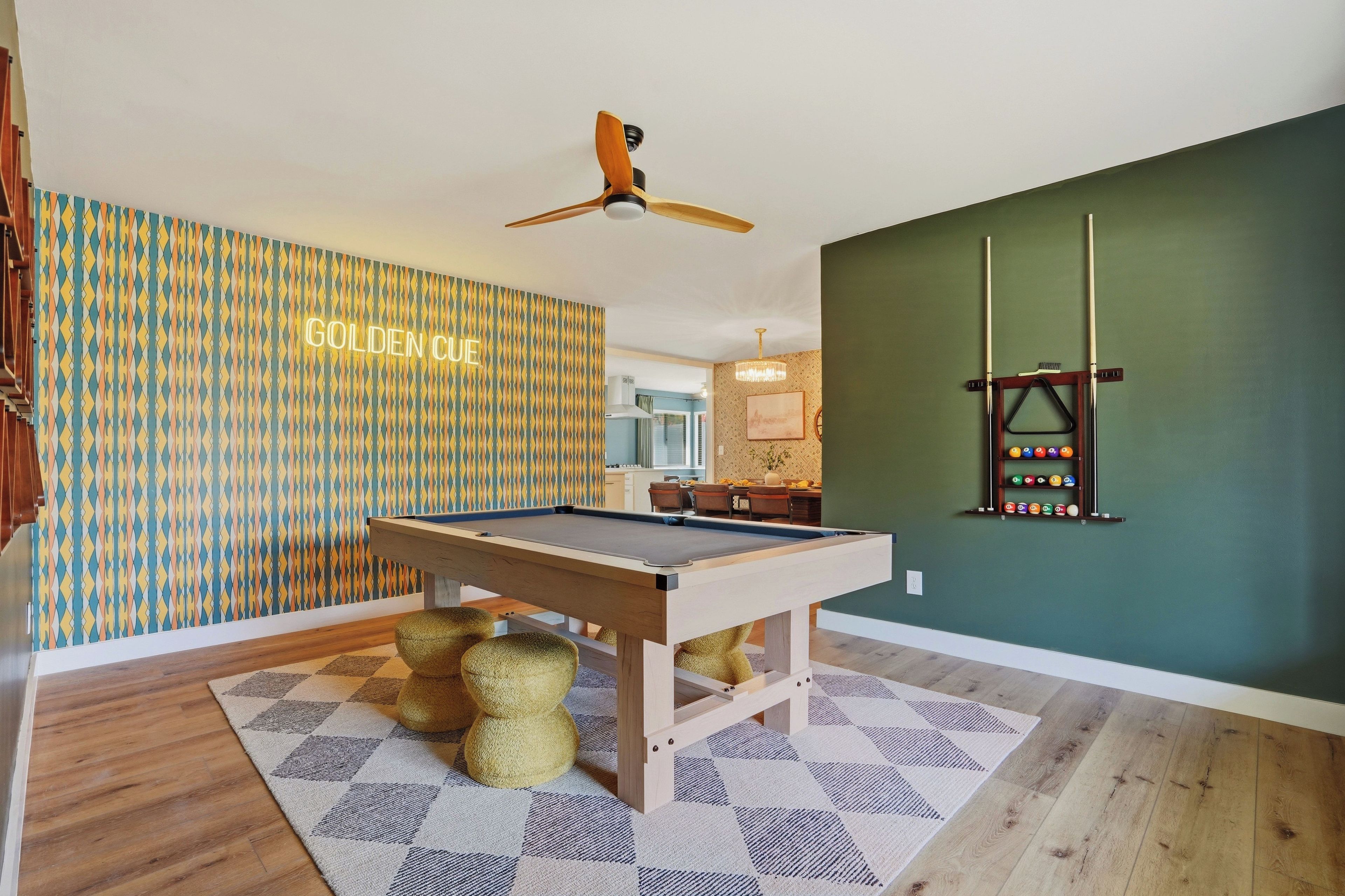 A pool table in a room with a patterned wall and a ceiling fan.