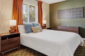 A hotel room with a large bed, two bedside tables with lamps, a nightstand, a headboard, and a wall-mounted artwork.