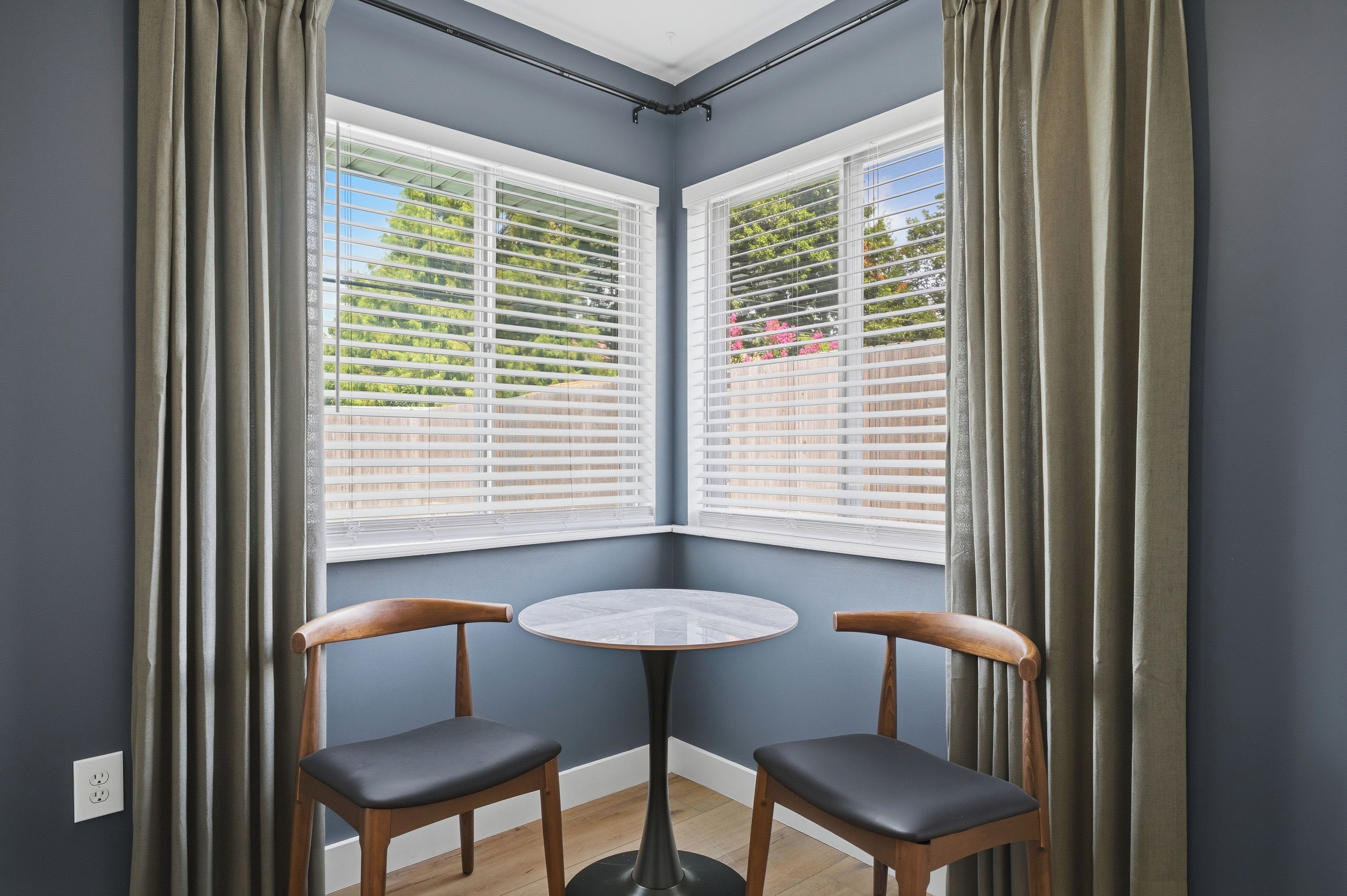 A corner room with two chairs, a small table, and a window with blinds.
