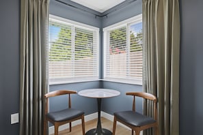 Ein Eckzimmer mit zwei Sessel, einem kleinen Tisch und einem Fenster mit Jalousien.