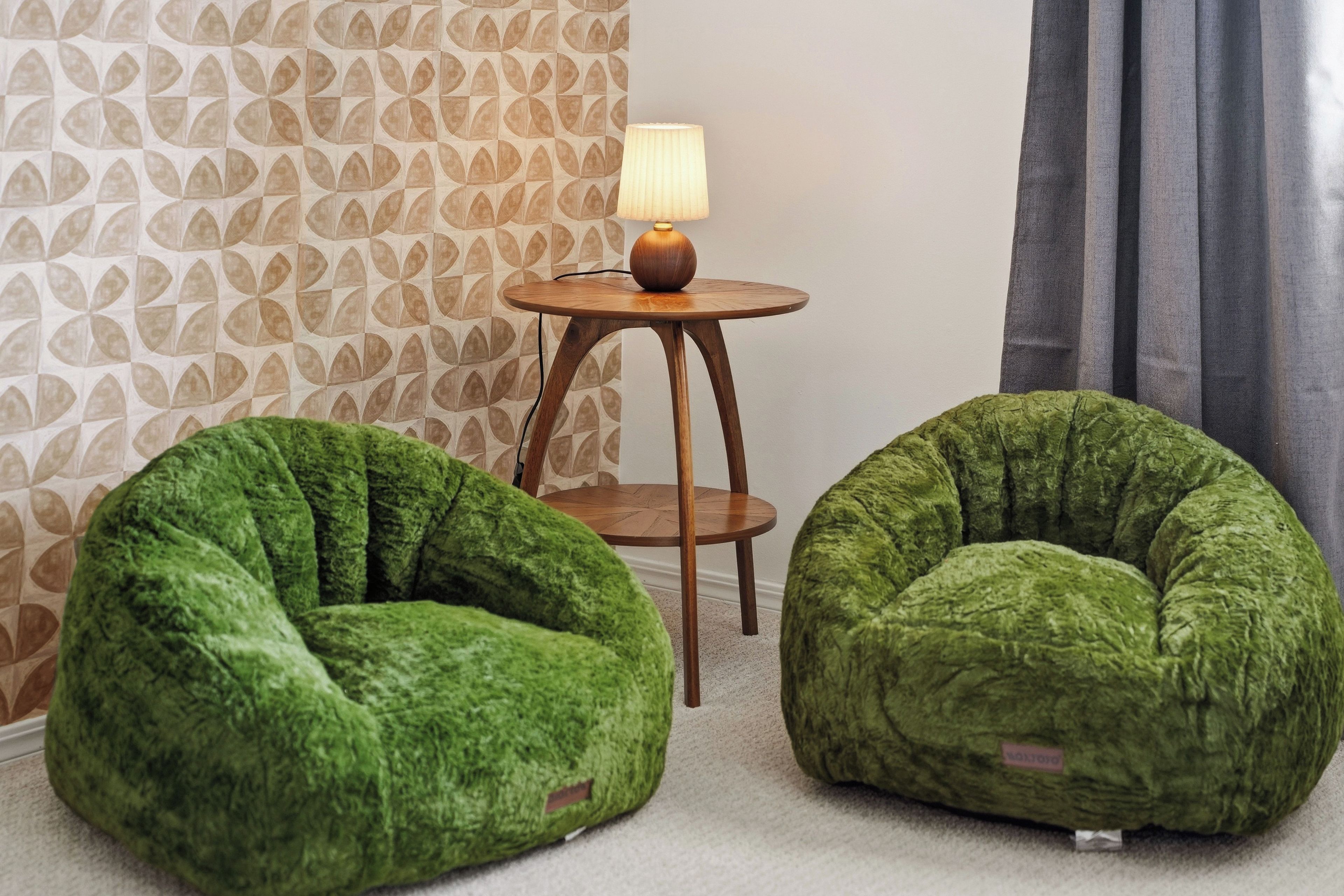 Two green bean bag chairs, a small wooden side table with a lamp, and a patterned wallpaper wall.