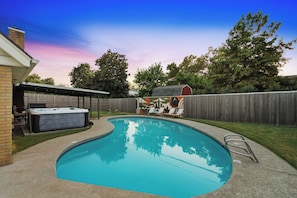 A backyard with a swimming pool, a hot tub, and a covered patio area.