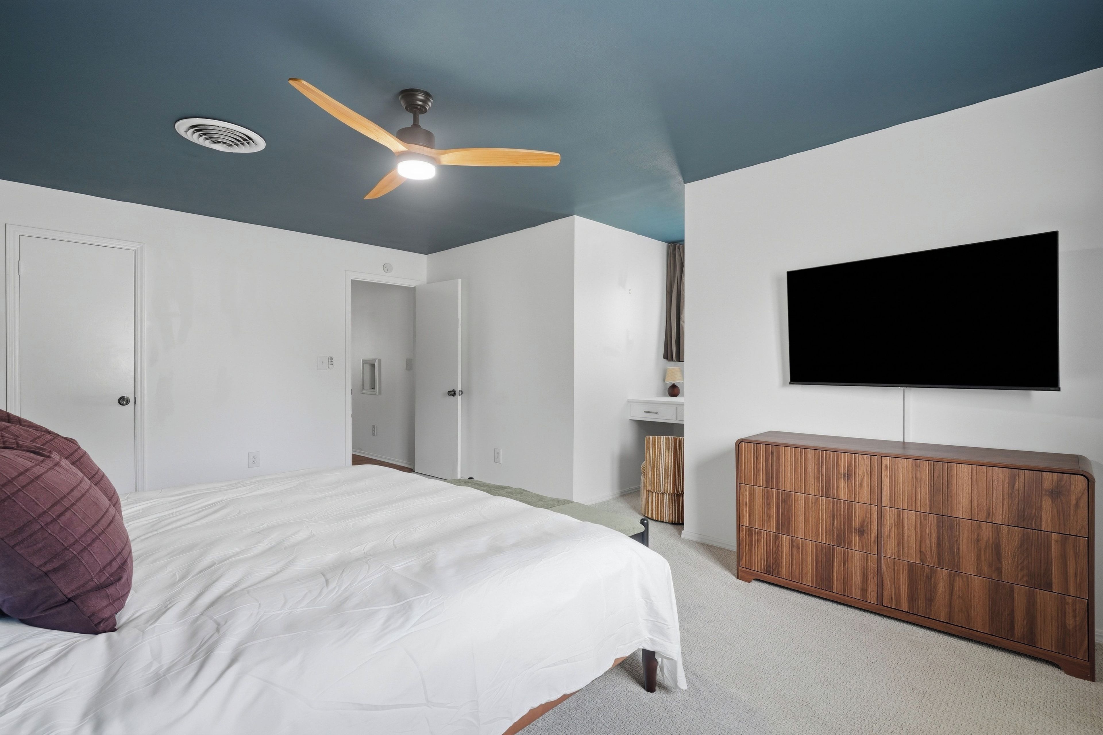 Un dormitorio con cama, un armario de madera, un ventilador de techo y un televisor montado en la pared.