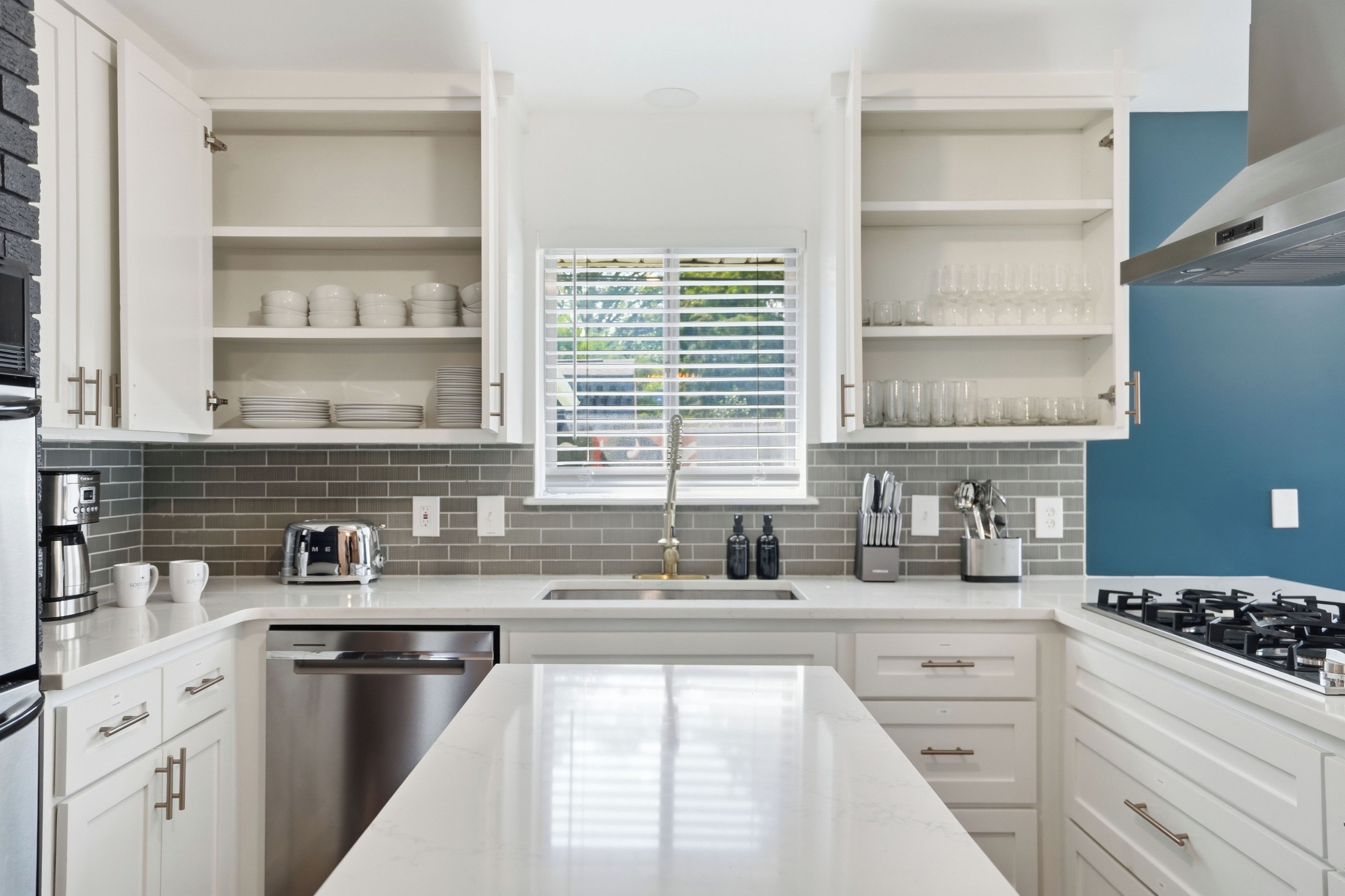 Una cocina moderna con armarios blancos, lavavajillas de acero inoxidable y estufa a gas.