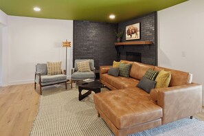 A living room with a brown leather sofa, two armchairs, a coffee table, a fireplace, and a green ceiling.