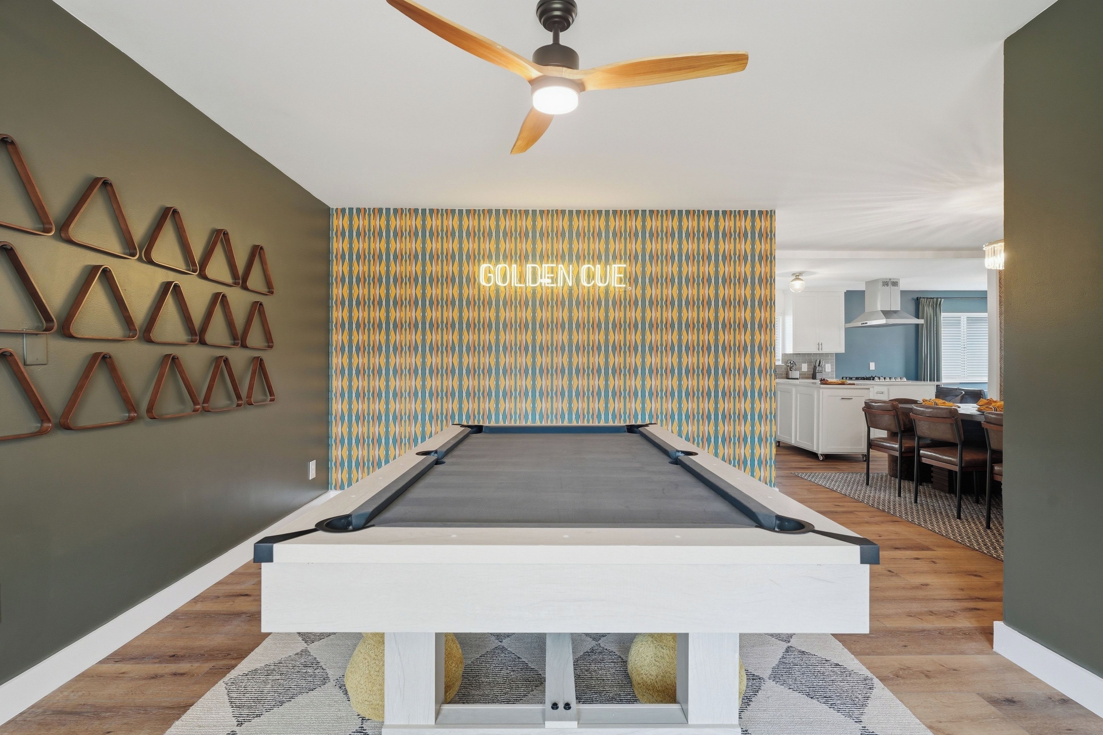 A pool table in a room with a patterned wall and a ceiling fan.