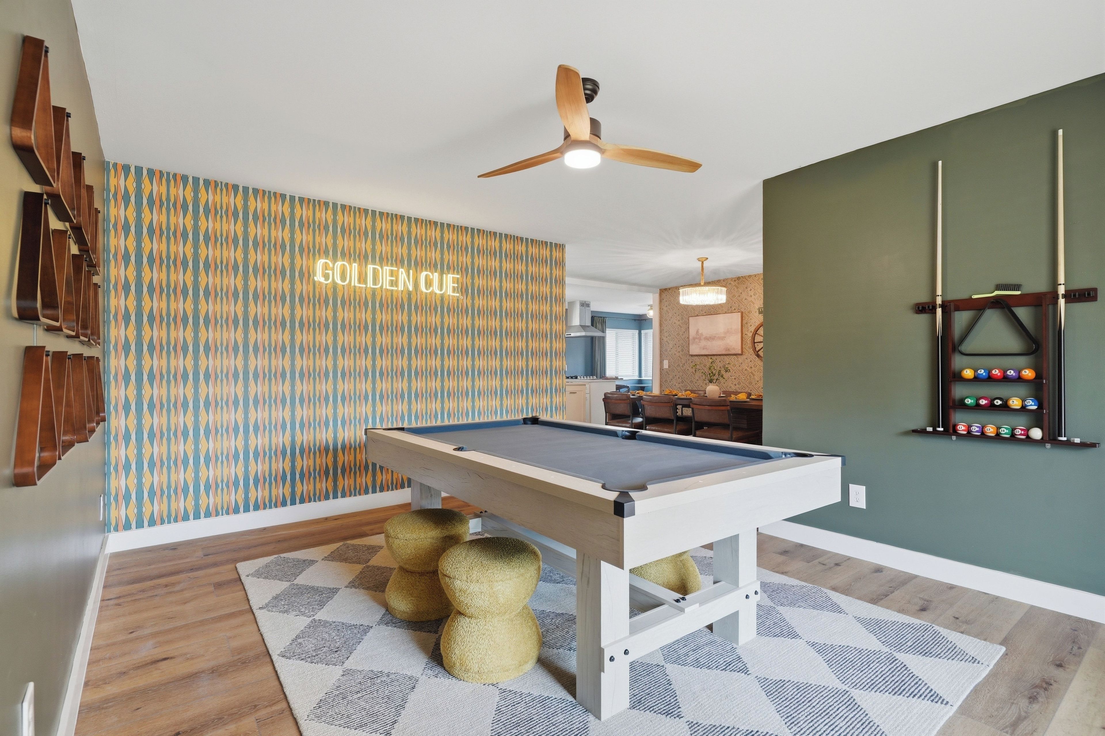 A pool table in a room with patterned wallpaper, a ceiling fan, and a billiards rack.