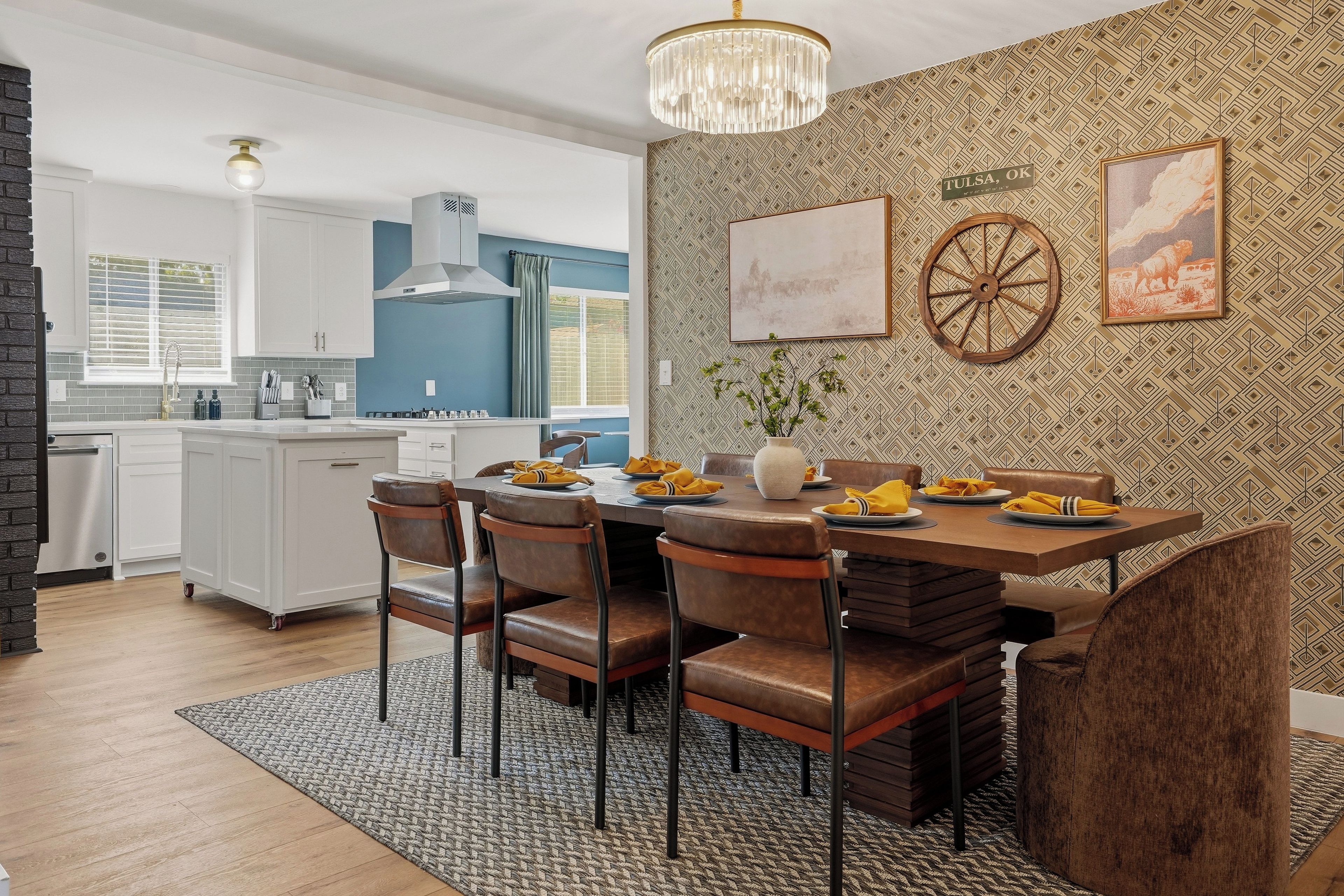 Una cocina moderna con armarios blancos, pared azul y una zona de comedor con mesa y sillas de madera.