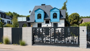 A modern two-story house with a blue facade, a gated entrance, and a metal fence with wildlife cutouts. - Baltic Villa - Sauna&Relax - Sobieszewo (Gdańsk)