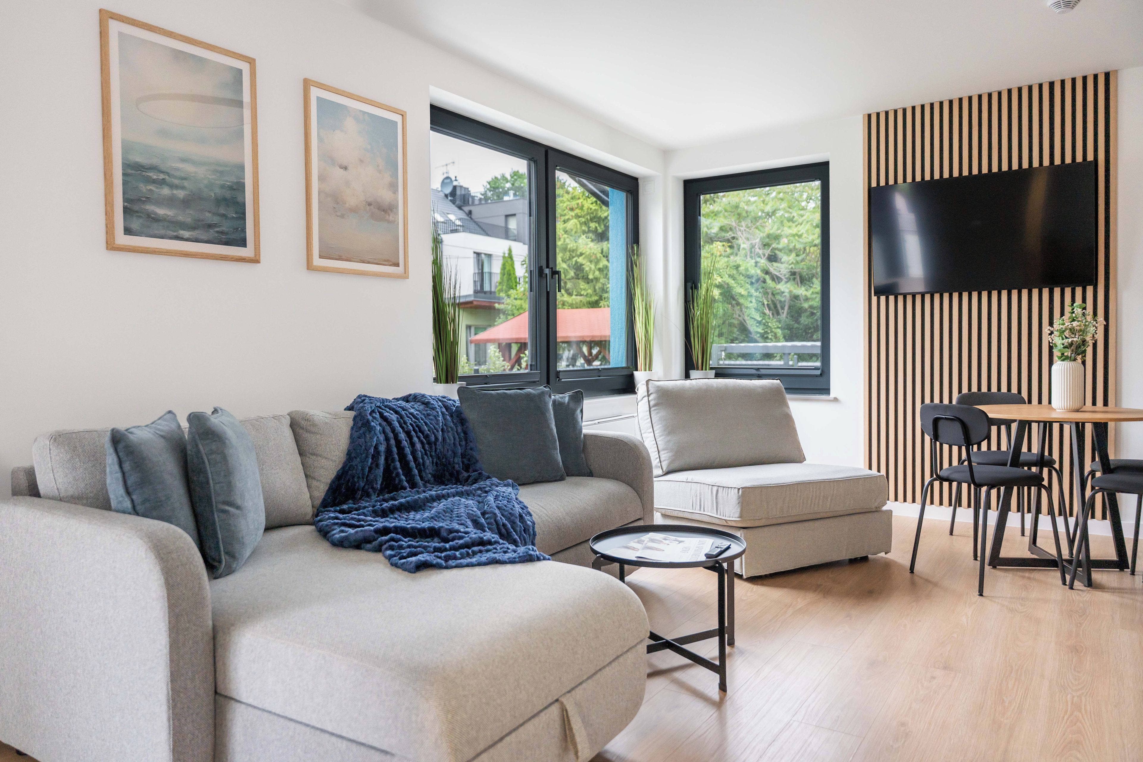 Ein modernes Wohnzimmer mit einer Couch, Sesseln, einem Couchtisch und einem an einer Wand montierten Fernseher, dessen Wandverkleidung ein Streifenmuster aufweist.