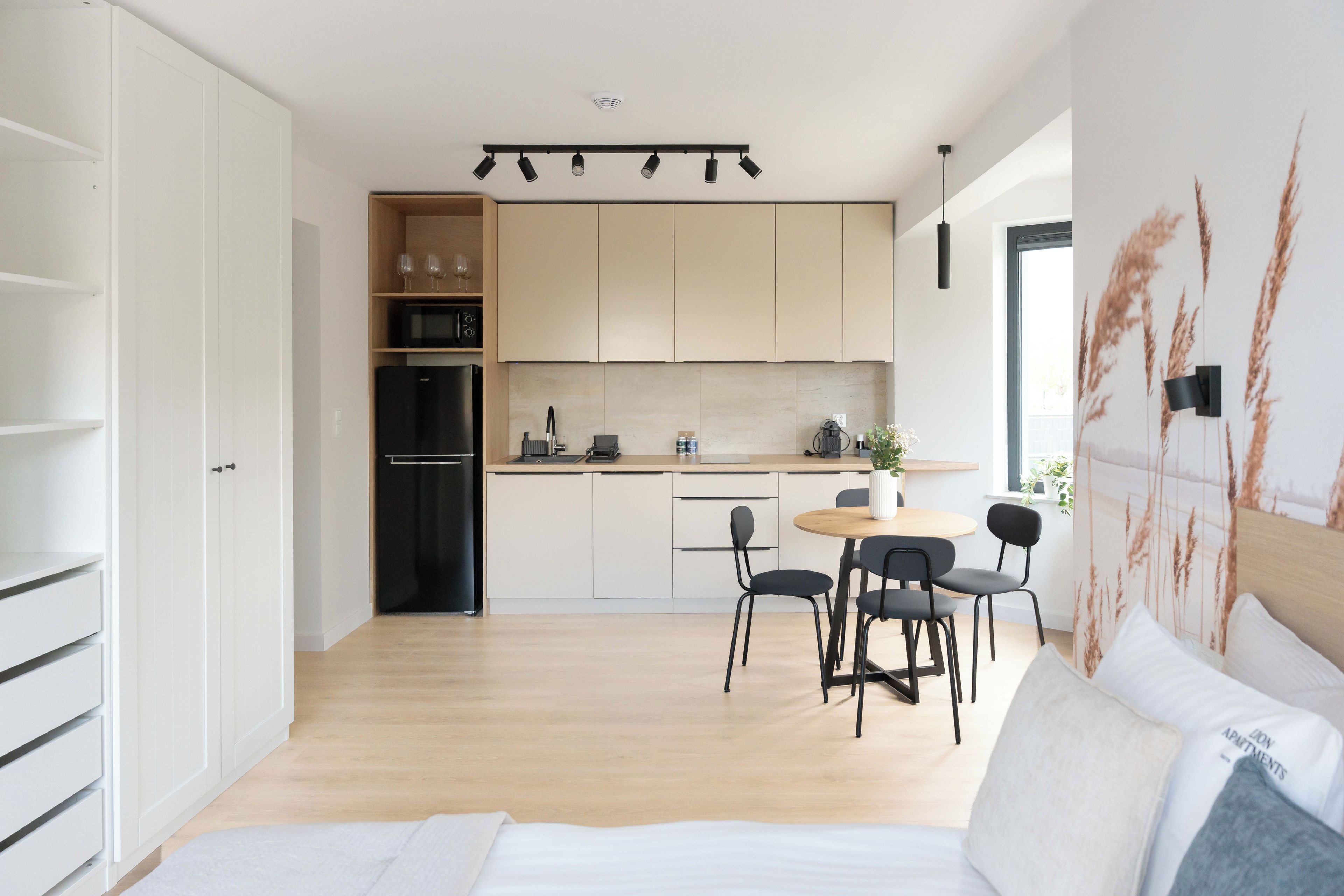 A modern kitchen with a dining area, wooden cabinets, a black refrigerator, and a dining table with chairs.