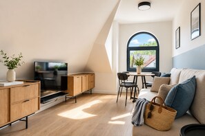 Uma sala de estar moderna com televisão, armários de madeira, espaço para refeições e uma janela grande.