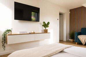 Quarto moderno com cama, TV na parede, mesa de cabeceira com planta e armário fixado na parede.