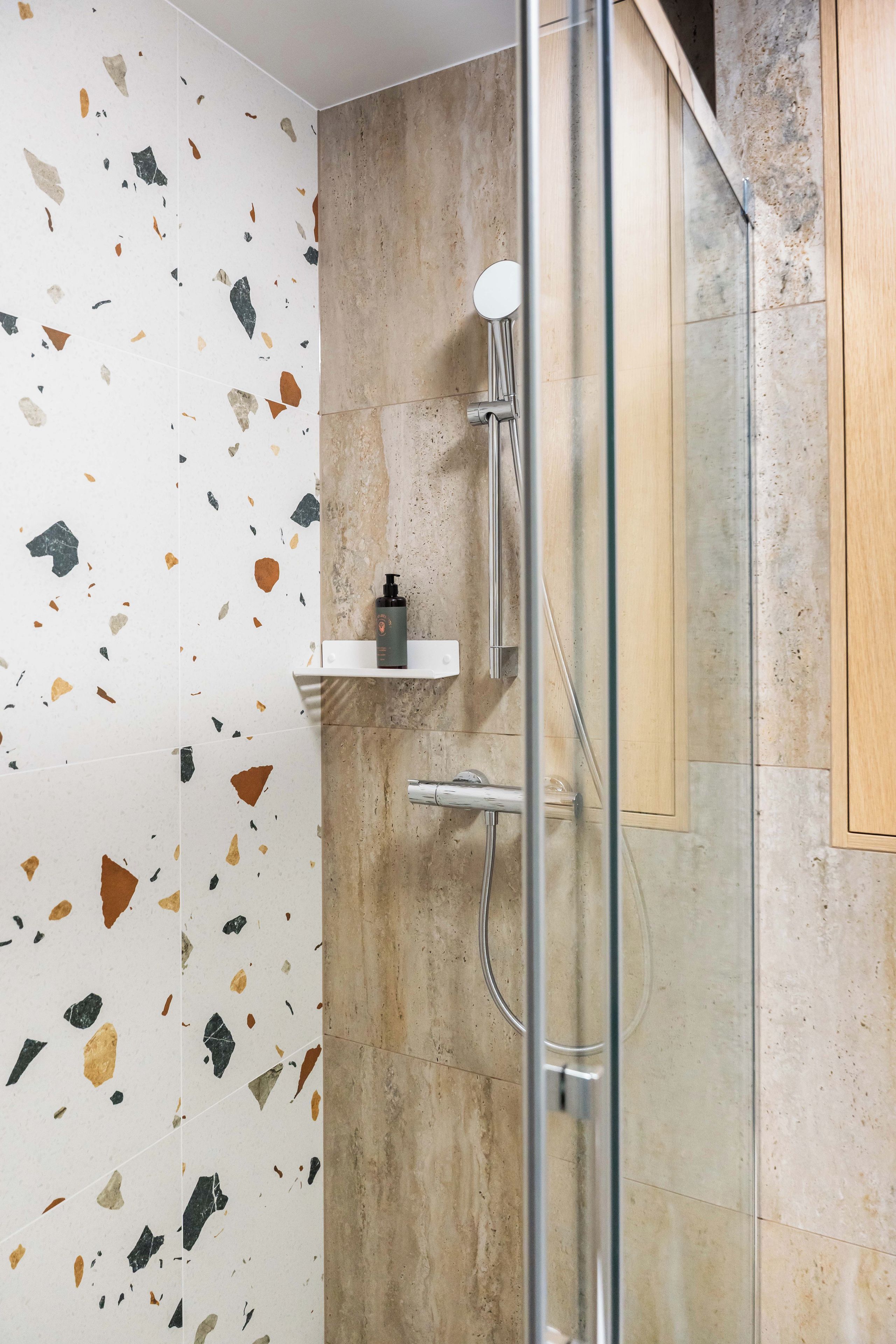 Un baño moderno con cabina de ducha de vidrio, pared con motas blancas y mueble de madera.