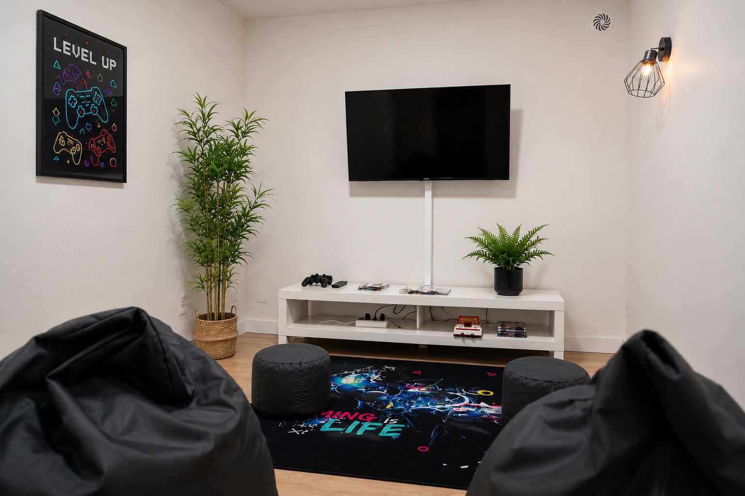 Una habitación con una televisión de pantalla plana montada en la pared, un mueble blanco con controles de videojuegos y una planta, además de una alfombra con temática de videojuegos.