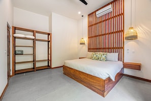 A bedroom with a wooden bed frame, a built-in wardrobe, a wall-mounted air conditioner, and two pendant lights. - Tamarindo Compound w/ Pools & Stunning Views (Tamarindo)