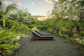 A secluded outdoor seating area with a lounge chair and a small table, surrounded by dense foliage and a gravel path. - Tamarindo Compound w/ Pools & Stunning Views (Tamarindo)