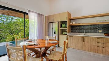 A modern kitchen with wooden cabinets, a dining area with a table set for four, and a view of lush greenery outside.