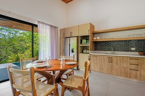 Une cuisine moderne avec des meubles en bois, un coin repas avec une table dressée pour quatre personnes, et une vue sur un paysage verdoyant.