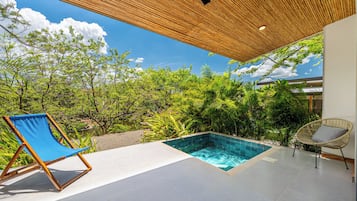 A pool area with a clear view of the sky, surrounded by lush greenery and a wooden pergola.