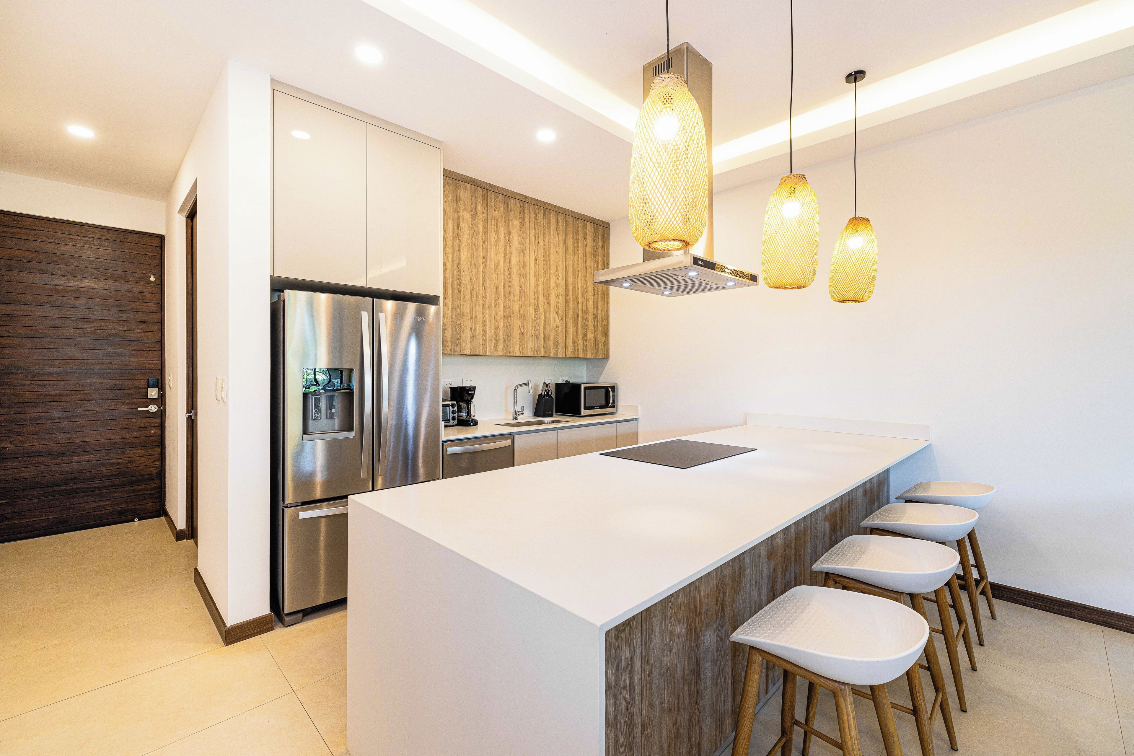 Une cuisine moderne dotée d’un grand îlot central, d’appareils électroménagers en acier inoxydable, de meubles en bois et de luminaires suspendus.