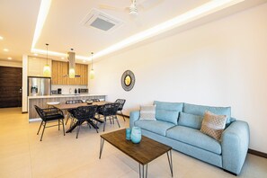 Ein modernes Wohnzimmer mit einer Couch, einem Couchtisch und einem Essbereich mit Stühlen sowie einer Küche im Hintergrund.