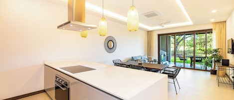 Une cuisine moderne dotée d’un îlot central, de luminaires suspendus et d’un coin repas offrant une vue sur l’extérieur.