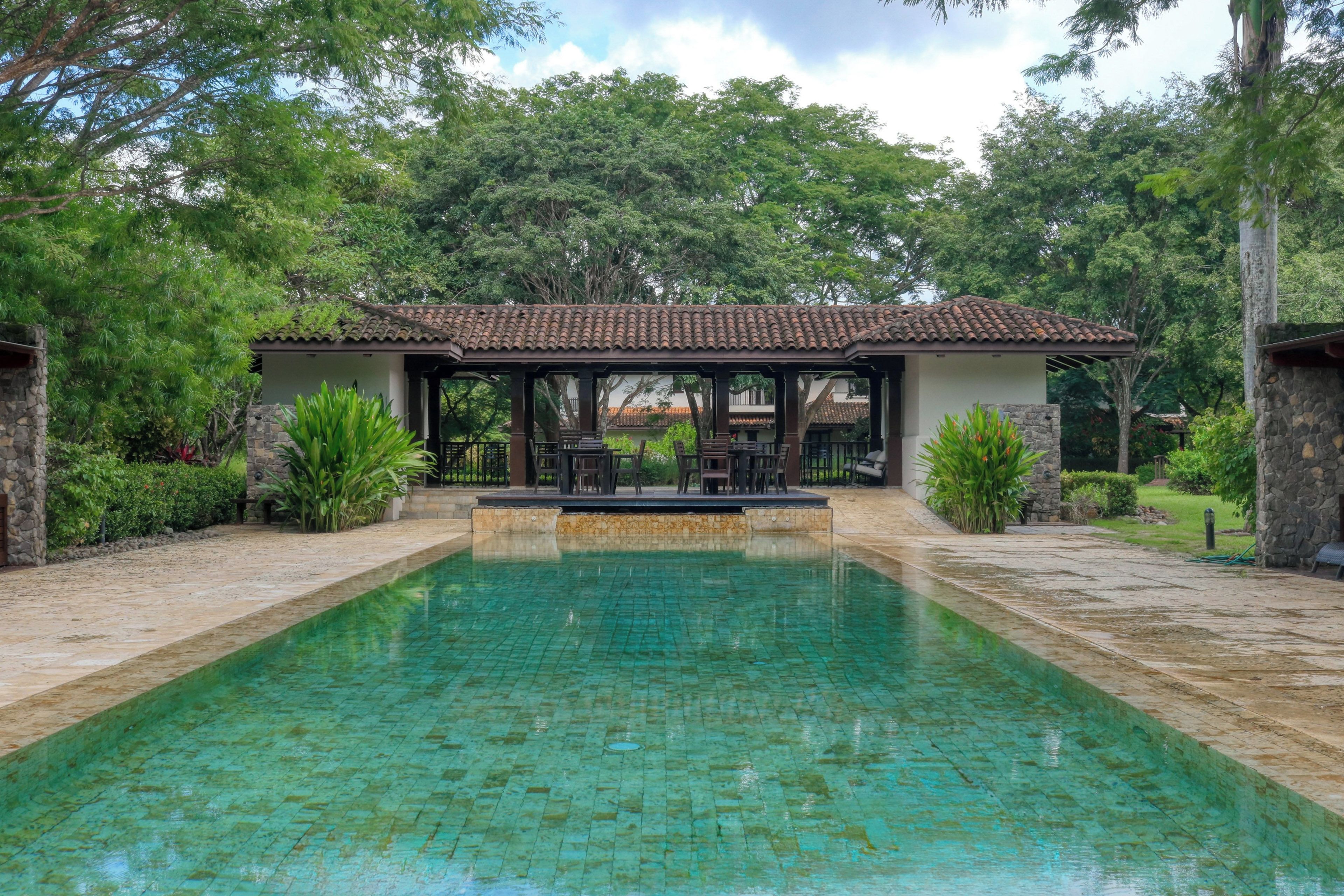 Une piscine rectangulaire, bordée d’une terrasse carrelée et entourée de murs en pierre et d’une végétation luxuriante.