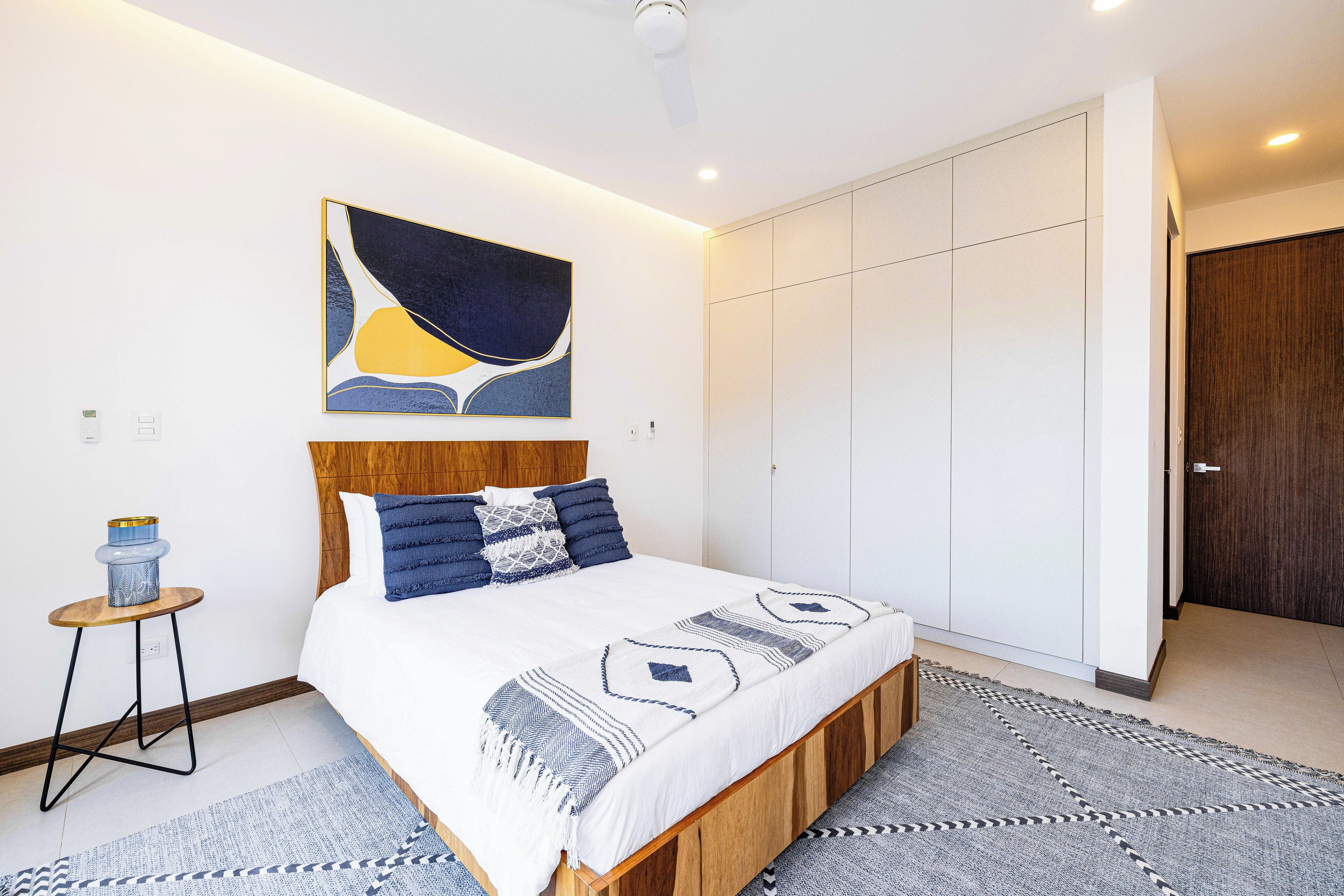 Une chambre à coucher moderne comprenant un lit, une table de chevet, une œuvre d’art accrochée au mur et une armoire.