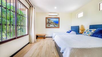 A hotel room with a large window, a painting, a bench, and a bed with pillows.