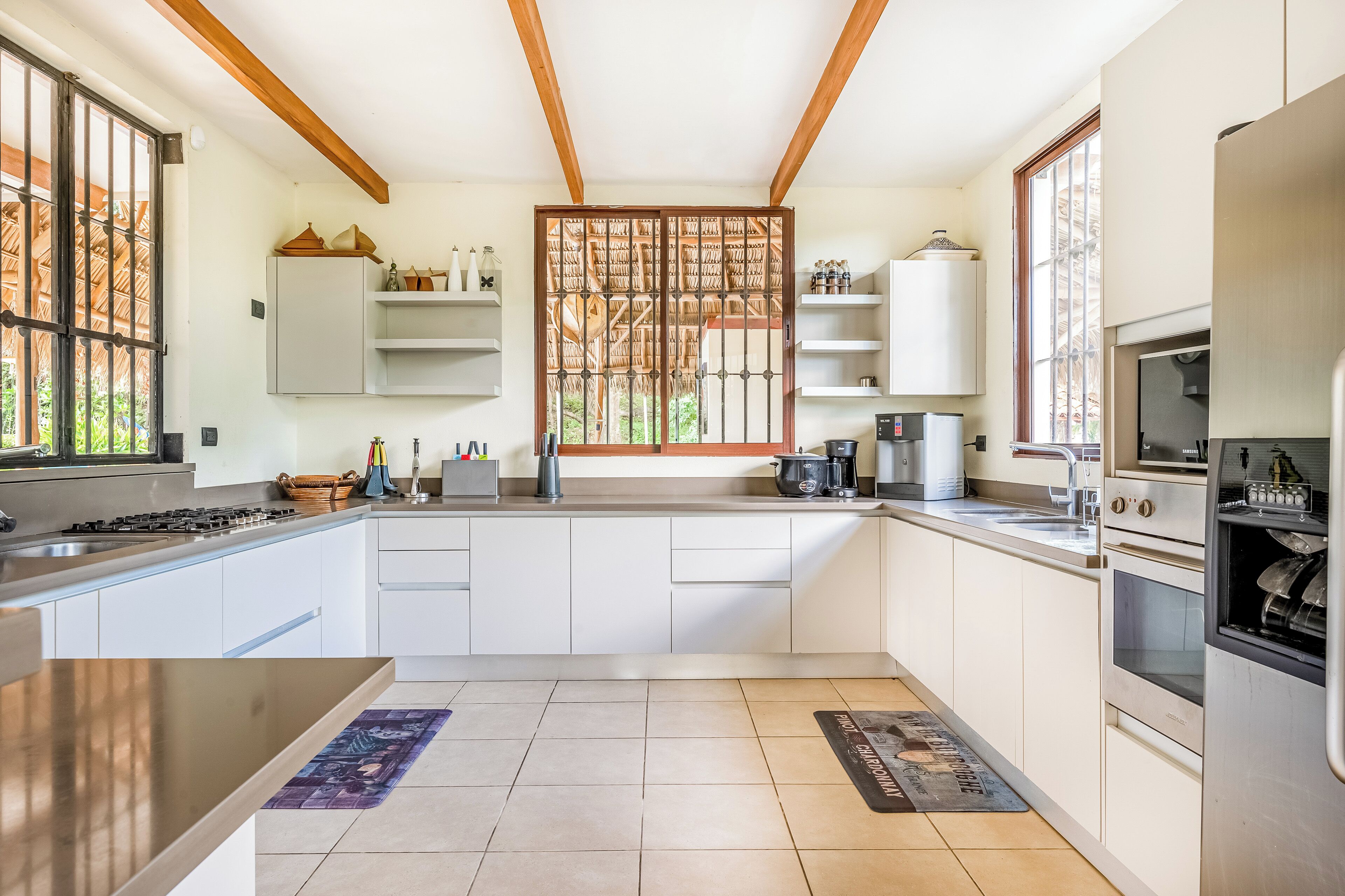 A modern kitchen with white cabinetry, a built-in oven, a coffee maker, and a window with a decorative screen.