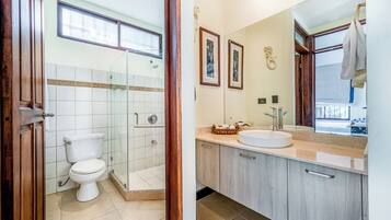 Une salle de bain comprenant des toilettes, une douche fermée par une paroi de verre, un lavabo et un miroir.