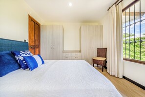 A bedroom with a bed, a chair, a wardrobe, and a window with curtains.