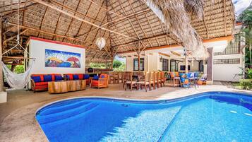Un área de piscina con techo de paja, asientos y una pintura.
