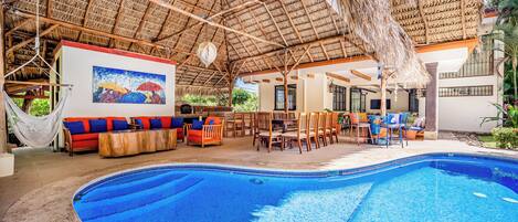 A pool area with a thatched roof, seating, and a painting.
