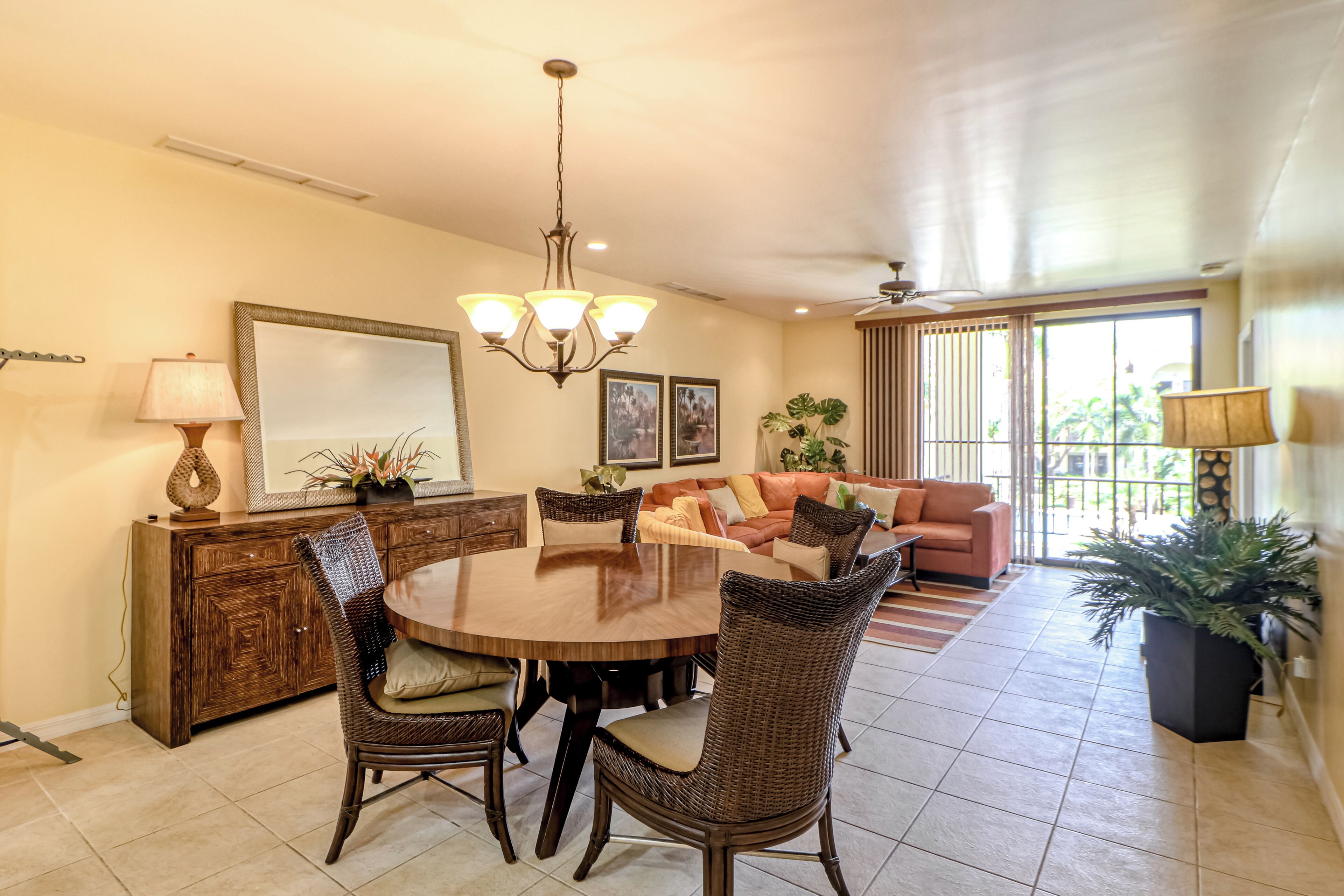 A dining area with a round table, chairs, a chandelier, a sofa, and a potted plant.