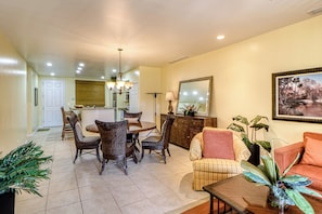A spacious living area with a dining table, chairs, a sofa, and a coffee table. There is a kitchen in the background, a large mirror on the wall, and a painting above the sofa. - Walkable Coco Beach Condo w/ Balcony, Pool (Sardinal)