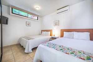 Habitación de hotel con dos camas, televisión, aire acondicionado y ventana con vista a árboles.