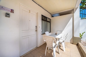 Una puerta blanca con un número, una ventana con cortinas, una mesa con sillas y un letrero sobre la puerta.